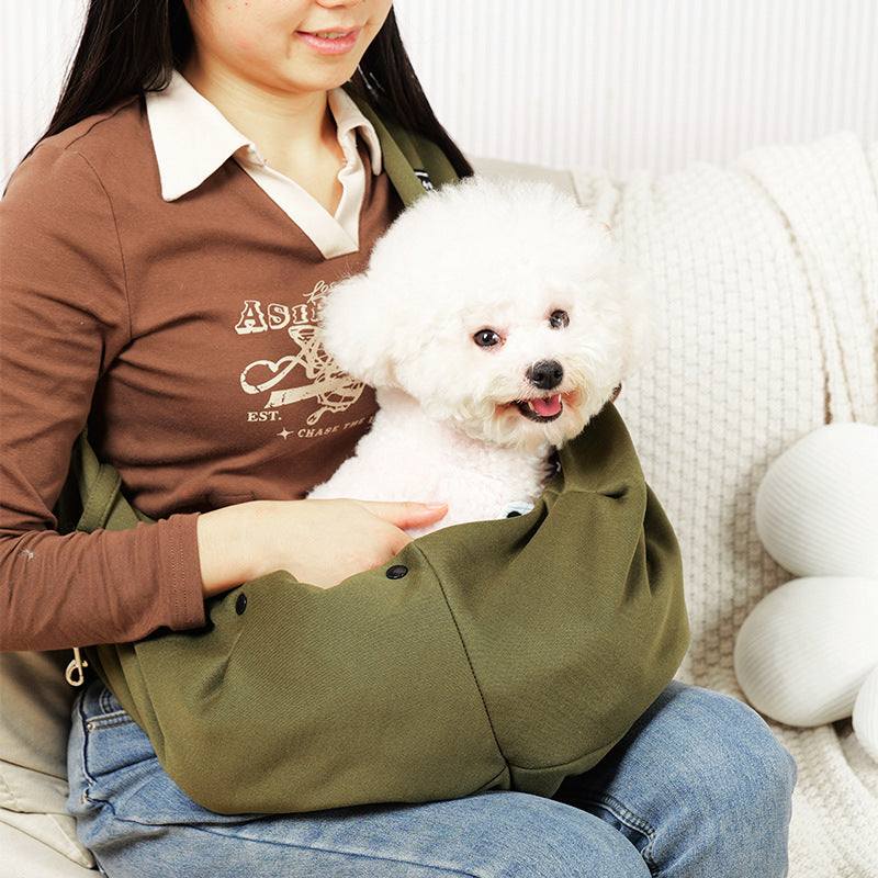 Bolsa de ombro para animais de estimação na cor verde-oliva, com um cachorro branco dentro, sendo segurada por uma mulher.