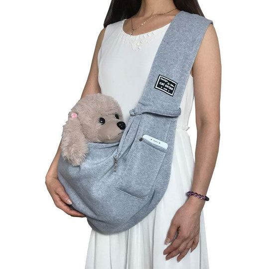 Bolsa de ombro cinza para pets, com bolso para celular e um cão de pelúcia acomodado na parte frontal.