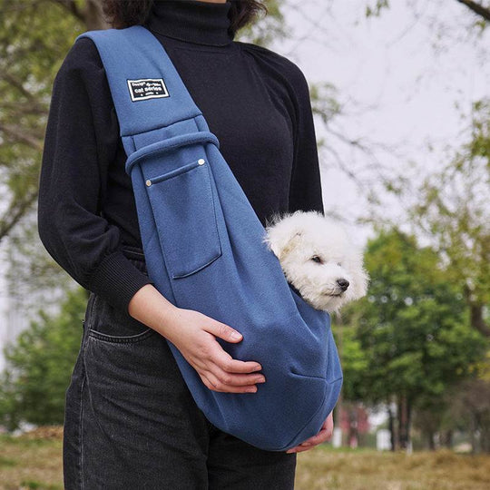 Bolsa de ombro azul para pets, com um cachorro branco saindo do bolso, material macio e design prático.