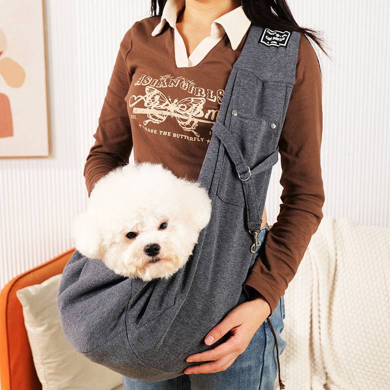 Bolsa de transporte cinza em tecido macio, utilizada como bolsa de ombro, com um cão dentro.