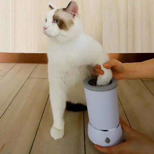 Limpa patas automático para animais. Equipamento branco, com uma mão segurando a pata do gato.